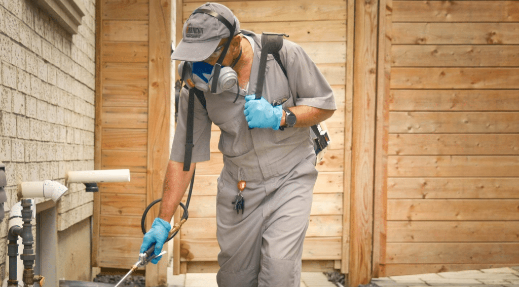 Pesticon technician applying exterior pest treatment around residential foundation